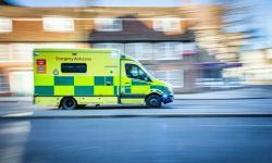Ambulance driving down a road with houses in the background.