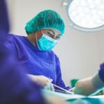 Medical professional in scrub cap performing a procedure.