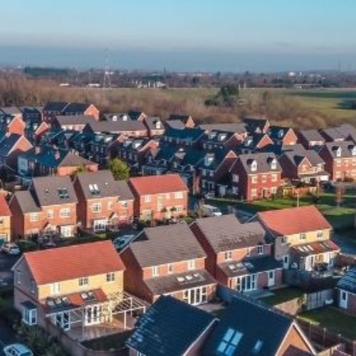 Aerial view photo of rows of houses, with grassy field in the background.